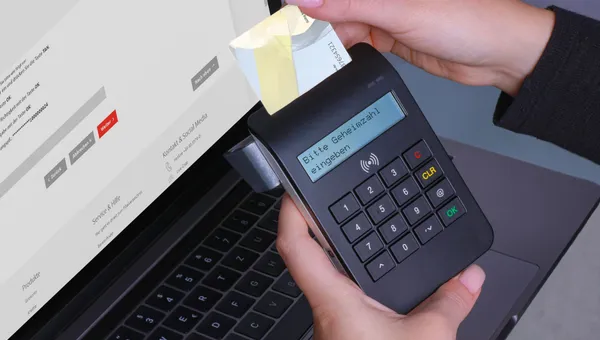 Eine Person verwendet ein Kartenlesegerät für eine sichere Online-Zahlung mit einem Laptop und PIN-Eingabe.