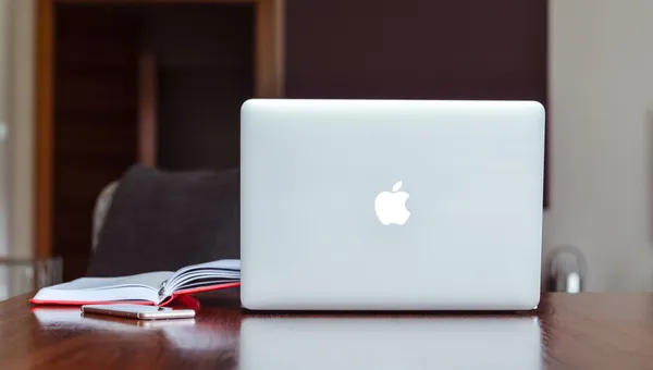 Ein sauberes und modernes Arbeitsumfeld mit einem Laptop, einem Buch und einem Smartphone auf einem Holztisch.