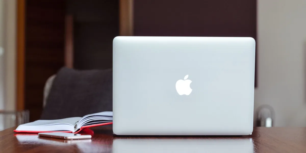 Ein sauberes und modernes Arbeitsumfeld mit einem Laptop, einem Buch und einem Smartphone auf einem Holztisch.