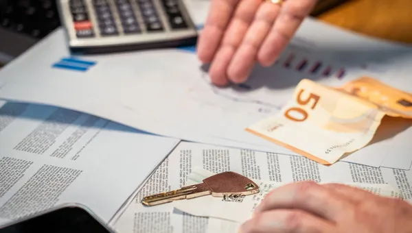 Hände, die Finanzdokumente, einen 50-Euro-Schein und einen Schlüssel überprüfen, was auf Investitions- oder Immobilienth