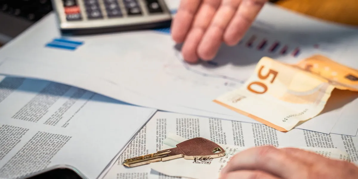 Hände, die Finanzdokumente, einen 50-Euro-Schein und einen Schlüssel überprüfen, was auf Investitions- oder Immobilienth