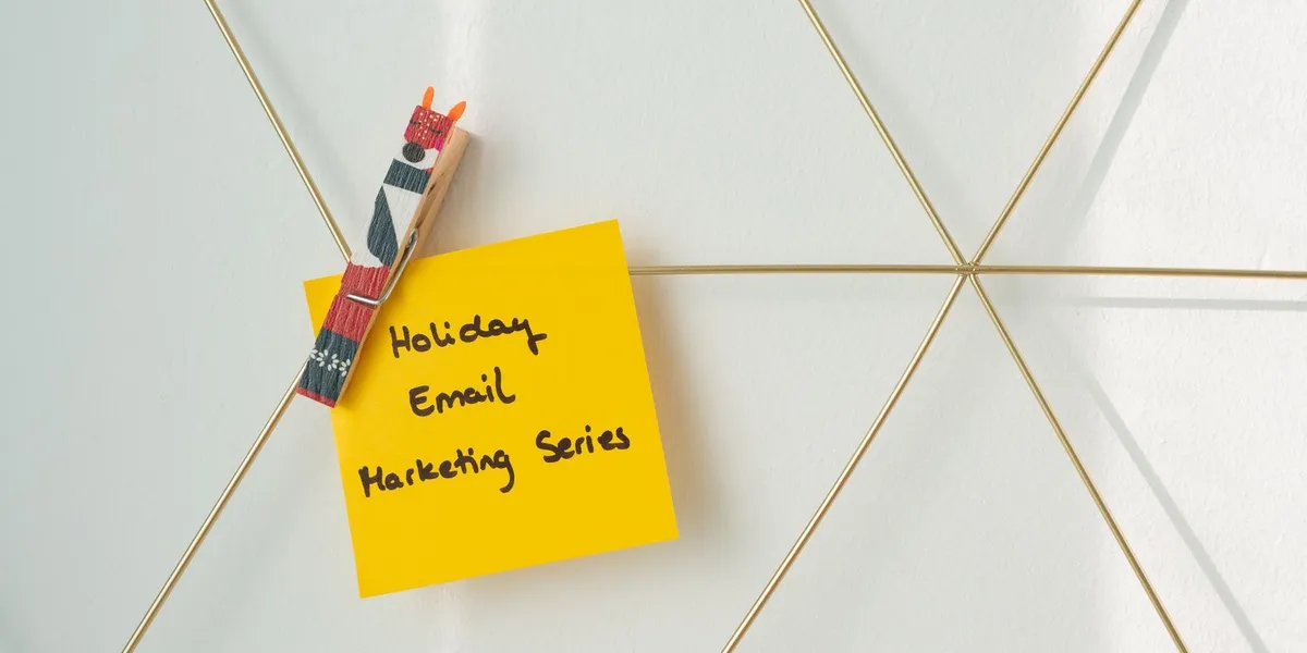 Helle gelbe Haftnotiz mit einer Urlaubs-Marketing-E-Mail-Nachricht an einer Drahtwand befestigt.