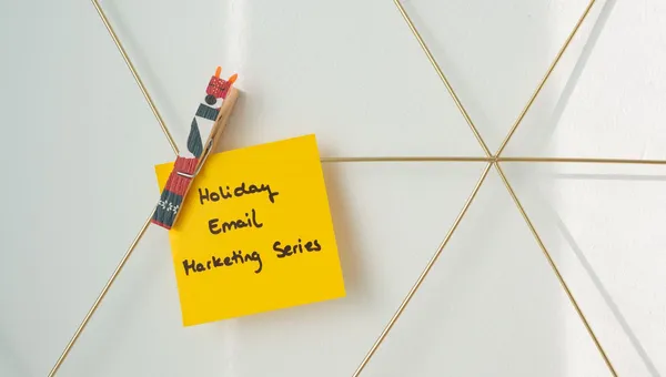 Helle gelbe Haftnotiz mit einer Urlaubs-Marketing-E-Mail-Nachricht an einer Drahtwand befestigt.