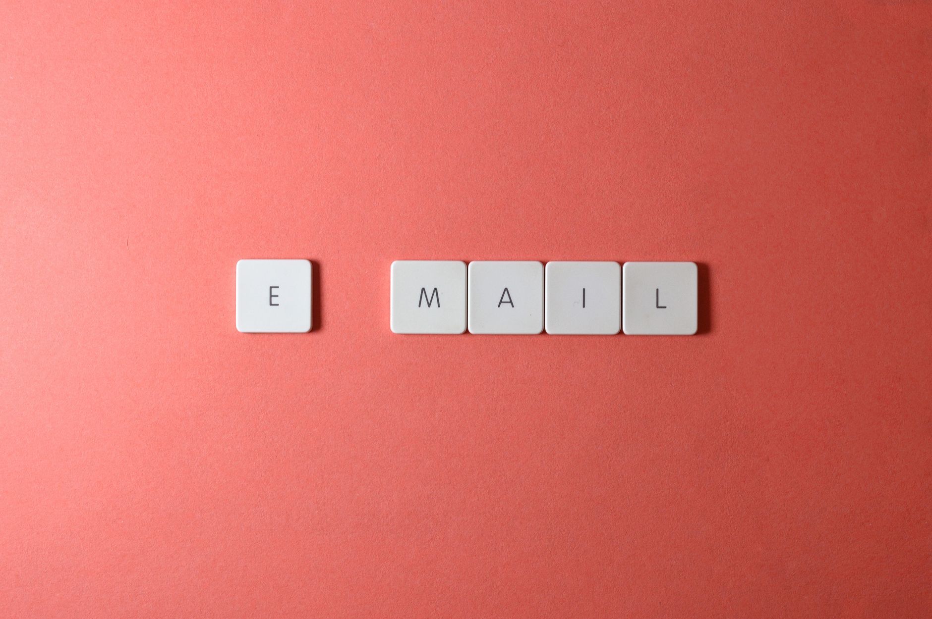 Draufsicht auf Buchstabentasten der Tastatur, die 'email' auf einem korallenfarbenen Hintergrund buchstabieren.